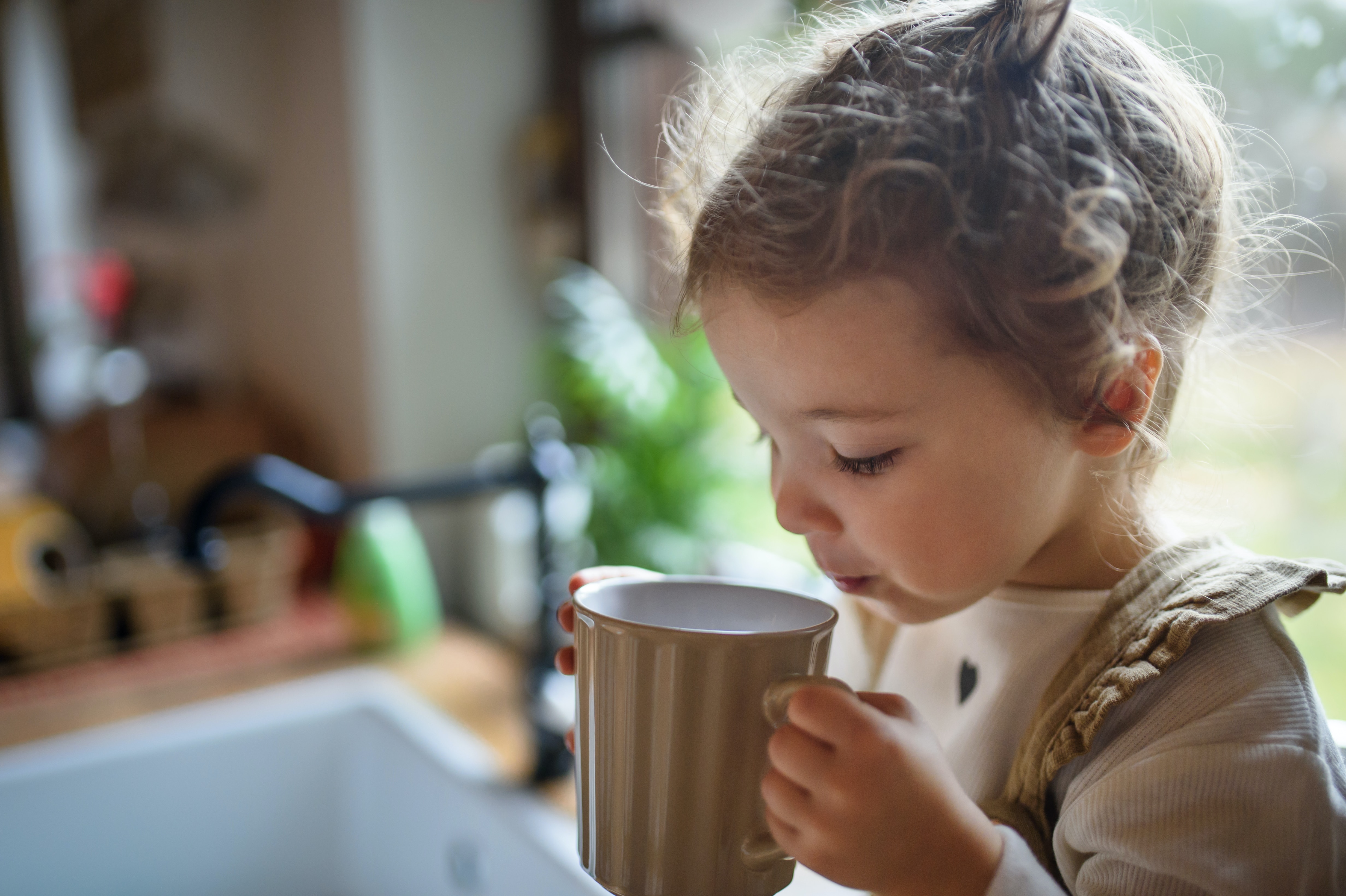 A young child holding a cup and preparing to drink from it.