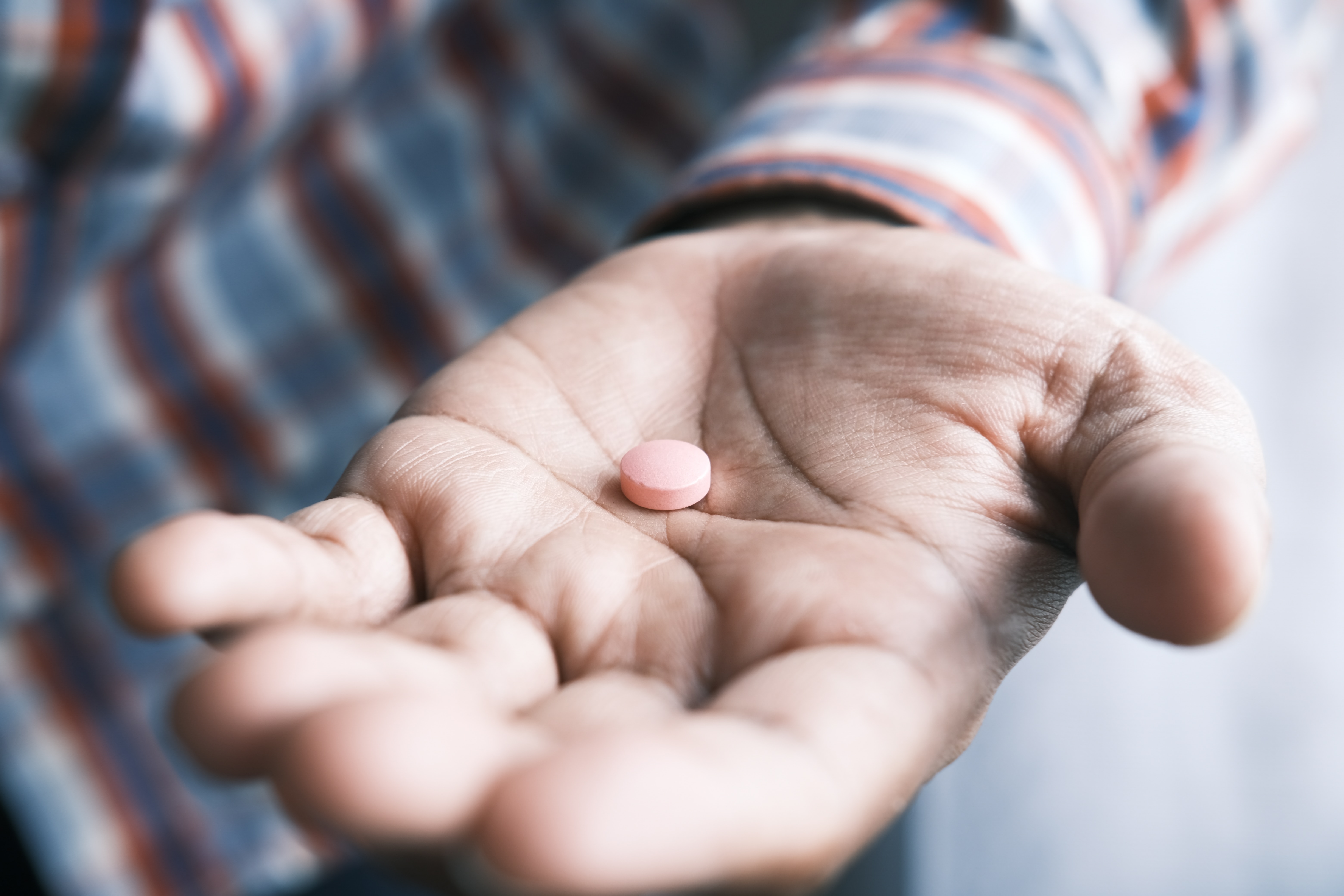 A child's open palm holding a small pink pill