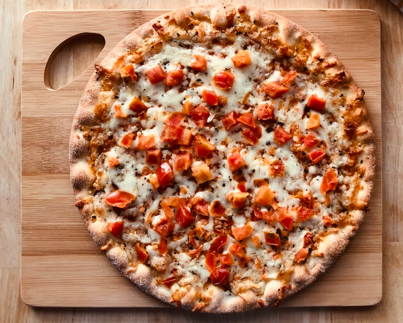 Freshly baked pizza with melted cheese and diced red peppers on a wooden serving board