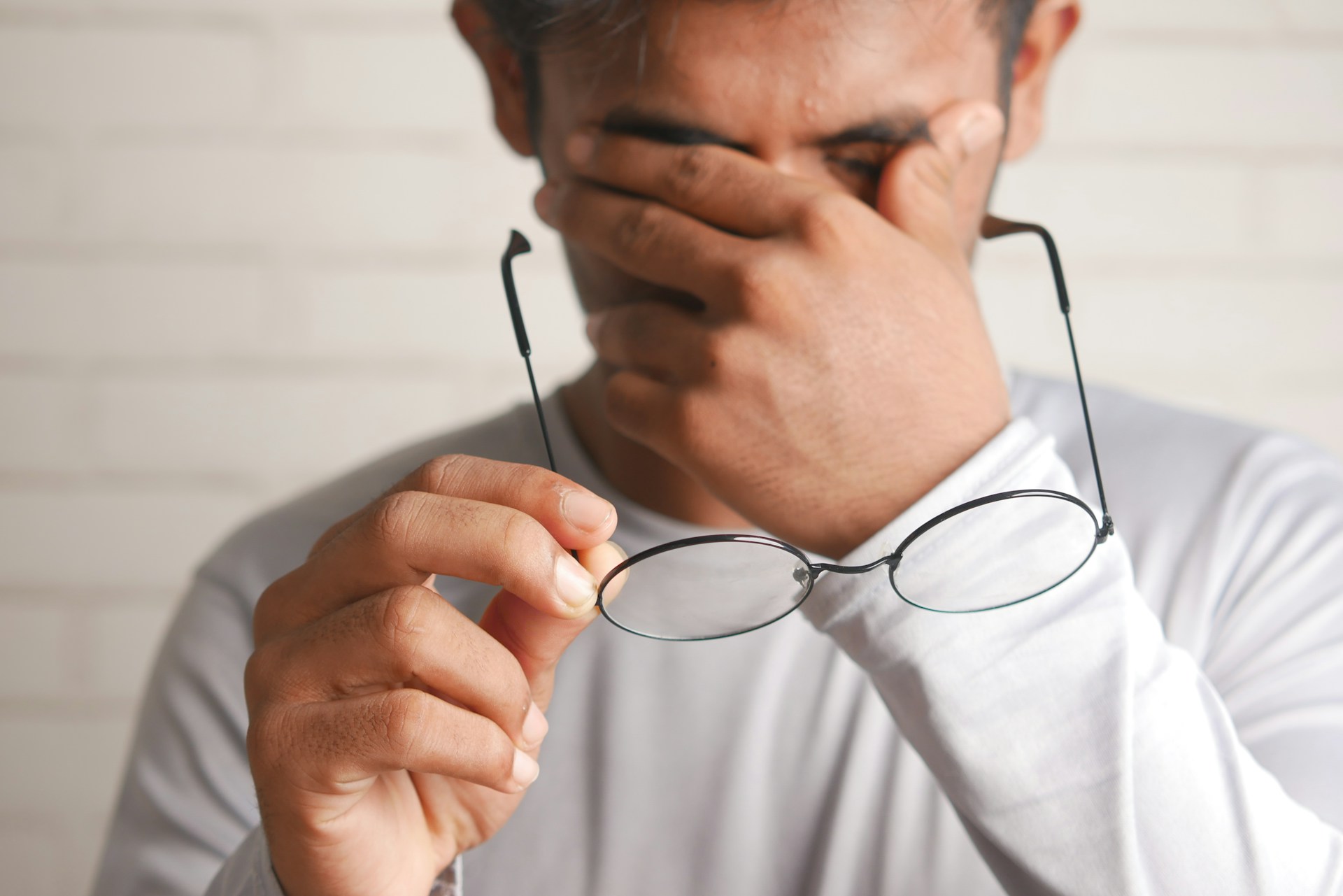 man holding glasses rubbing his eyes