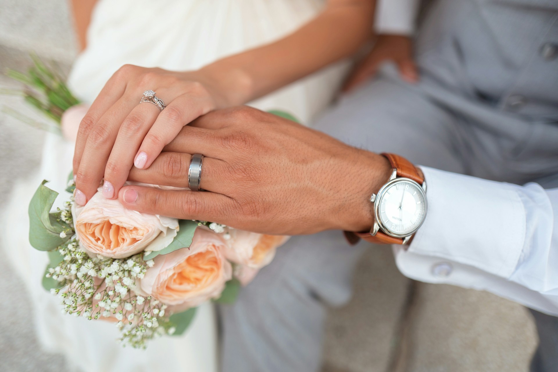 married couple's hands on bouquet