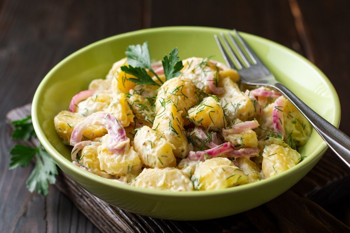 Potato salad with red onion and greens in bowl
