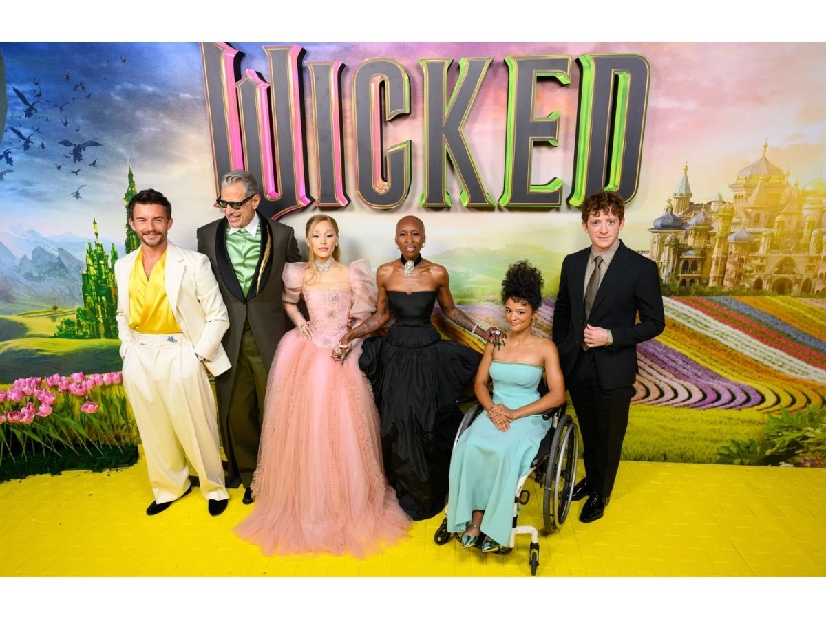 Wicked cast on the red carpet taking a photo together: includes Ariana Grande and Ethan Slater. Photo is before the celebrity couple broke up