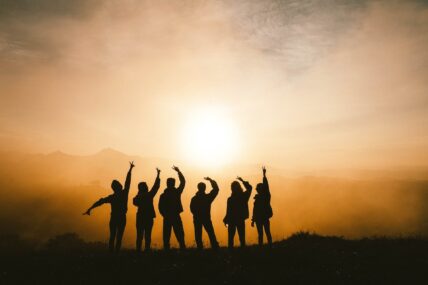 Silhouettes of six people with raised arms standing against a golden sunset