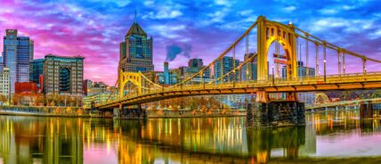 Yellow Sixteenth Street Bridge spanning the Allegheny River with Pittsburgh skyline at sunset