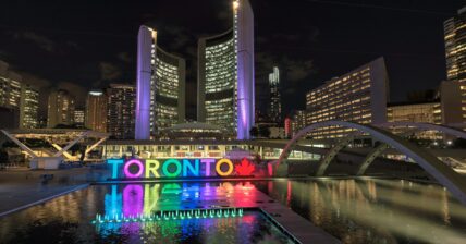 Toronto sign illuminated at night in Nathan Phillips Square with reflecting pool and city skyline
