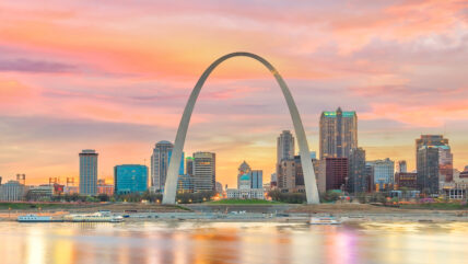Gateway Arch in St. Louis at sunset with city skyline and riverboat