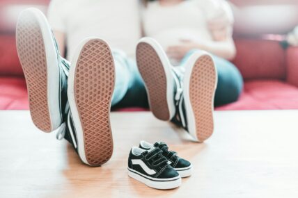Two adults and a child wearing sneakers lying on a pink mat indoors