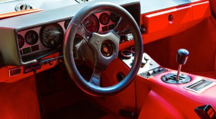 Bright red vintage car interior with steering wheel and dashboard gauges from the 1980s era