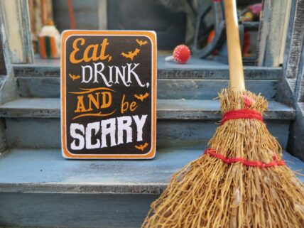 Halloween sign with "Eat, Drink, and be Scary" text next to a decorative witch's broom