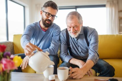 Young man pouring tea while sitting with an older man on a yellow couch