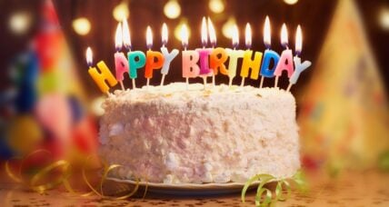 Colorful birthday cake with lit candles and "Happy Birthday" lettering on pink frosting