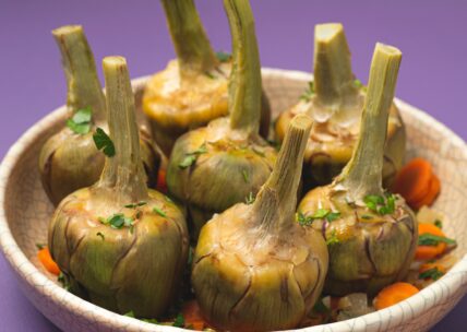 Cooked artichokes with stems intact garnished with parsley and carrots in a white bowl